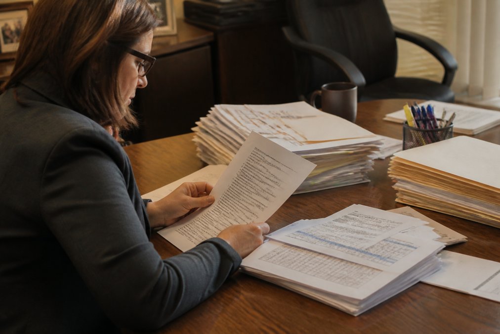 A loan officer reviewing a stack of financial documents and a court judgment notice at a desk under warm office lighting, with a computer screen showing a credit report