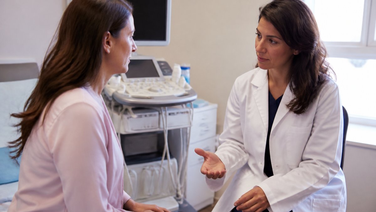 Female patient in consultation room with gynaecologist consultant, ultrasound equipment visible in background, professional clinical setting with soft natural lighting conveying reassurance