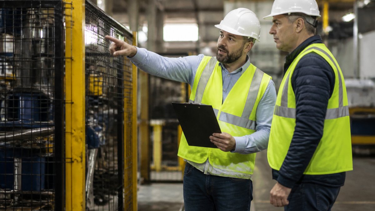 EHS consulting professional and plant manager reviewing machine guarding on a manufacturing floor.