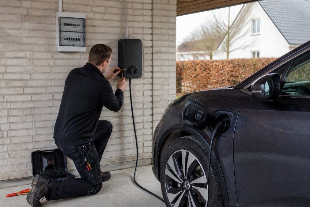 Ein zugelassener Elektriker installiert in der Garage einer dänischen Villa eine bidirektionale Ladebox neben einem Elektroauto.