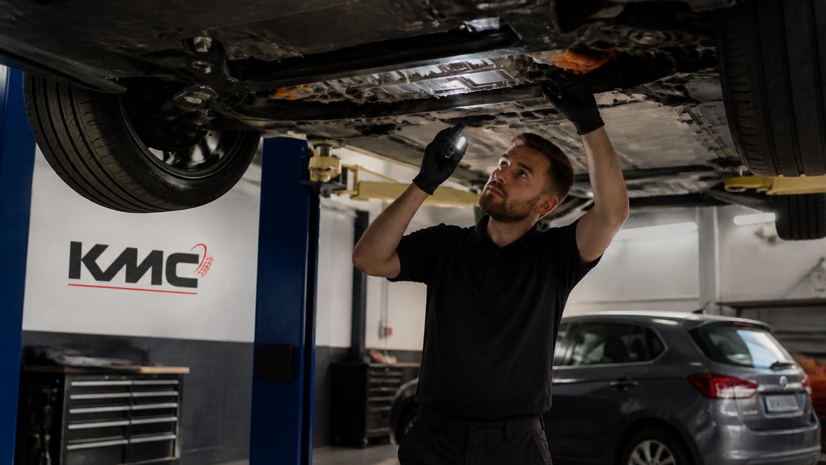 Professional mechanic performing visual inspection of electric vehicle's undercarriage and high-voltage battery connections during MOT test in modern service bay