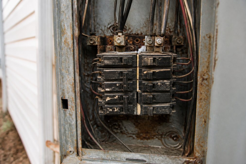 Close-up of an old, corroded electrical breaker box with worn components, visible rust, and deteriorating metal connections showing the condition of aging electrical infrastructure
