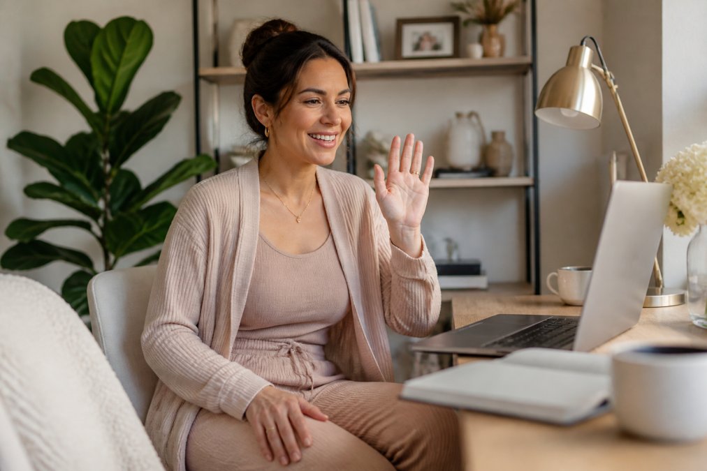 Woman styled in matching loungewear set with layered cardigan and minimal jewelry, seated at home office desk during video call with professional lighting