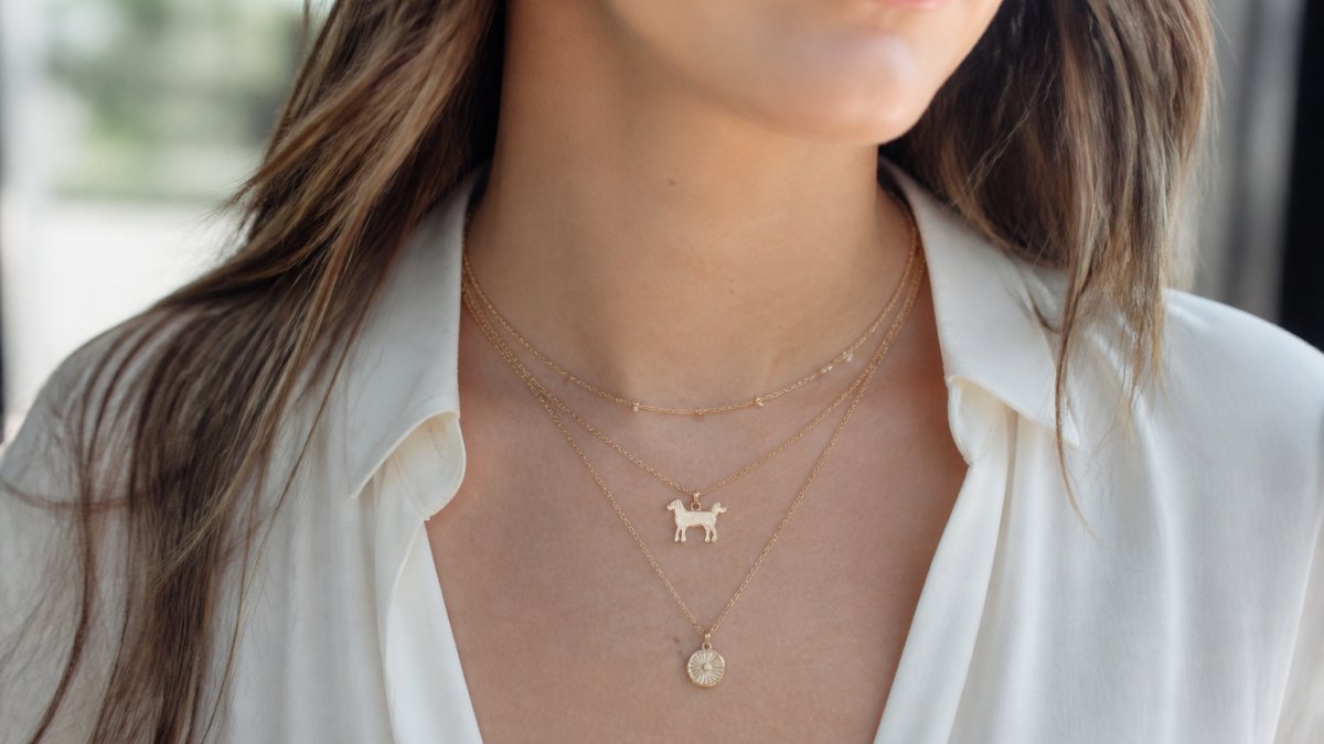 Woman wearing a delicate dog-themed necklace layered with other fine jewelry in soft natural light, showing how the piece integrates seamlessly into a polished everyday outfit