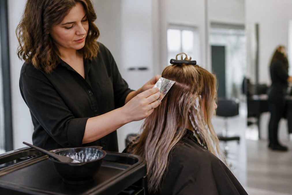 A professional colorist carefully performing a secure foil application on a client’s hair in a salon.