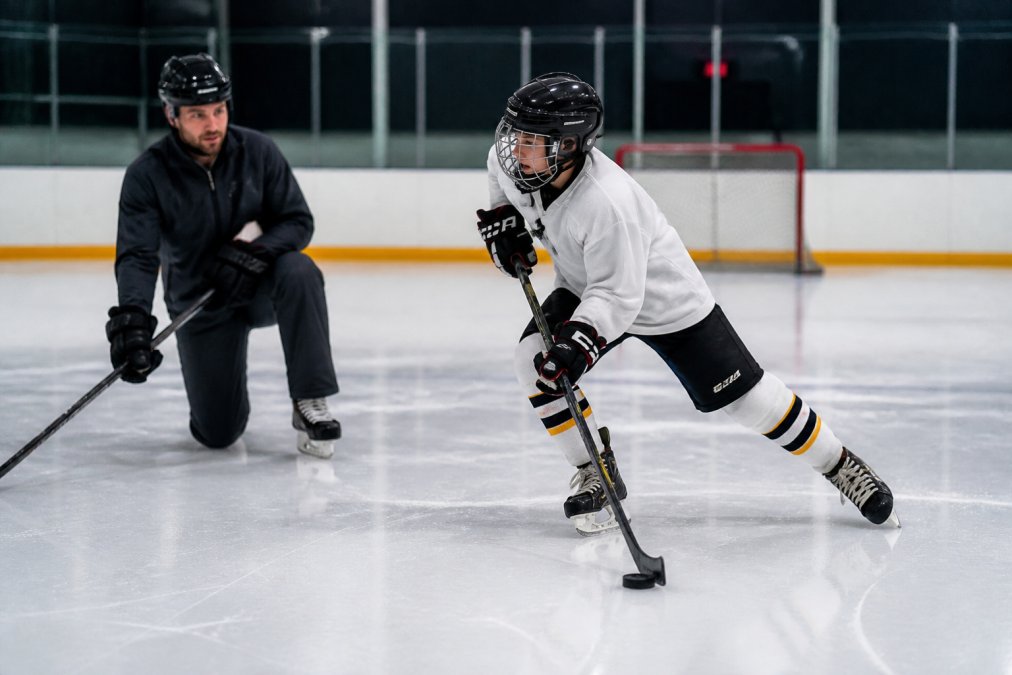 A coach instructs a young player on edge work during hockey skill sessions on the ice.