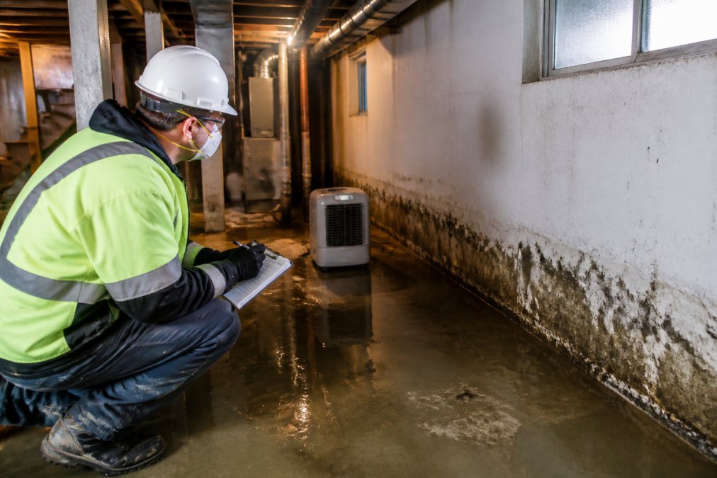 Homeowner in safety gear assessing water damage during emergency basement waterproofing efforts