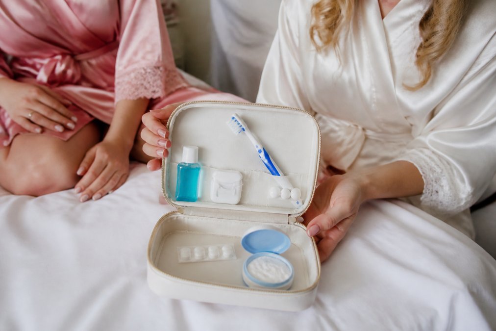 Close-up of a bride's hand holding a small emergency dental kit with disposable toothbrush, mouthwash, dental floss, breath mints, and temporary filling material arranged neatly on white fabric
