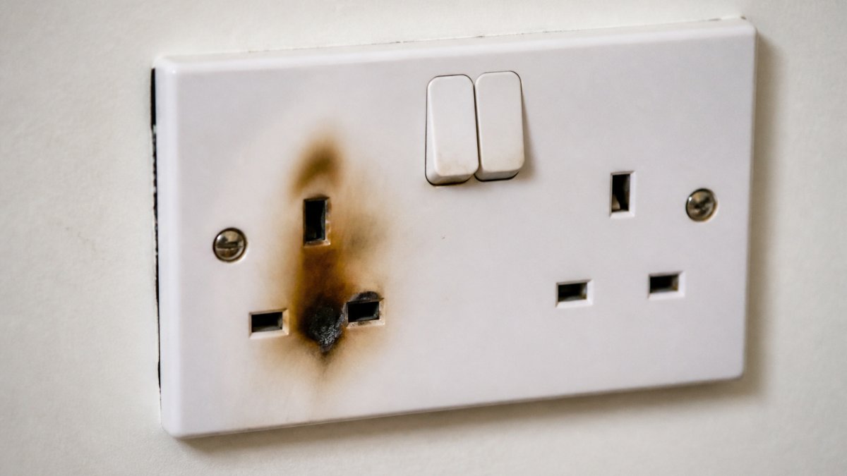 Close-up of a faulty electrical socket with visible scorch marks and discolouration around the outlet, demonstrating visible damage from electrical arcing, photographed in daylight
