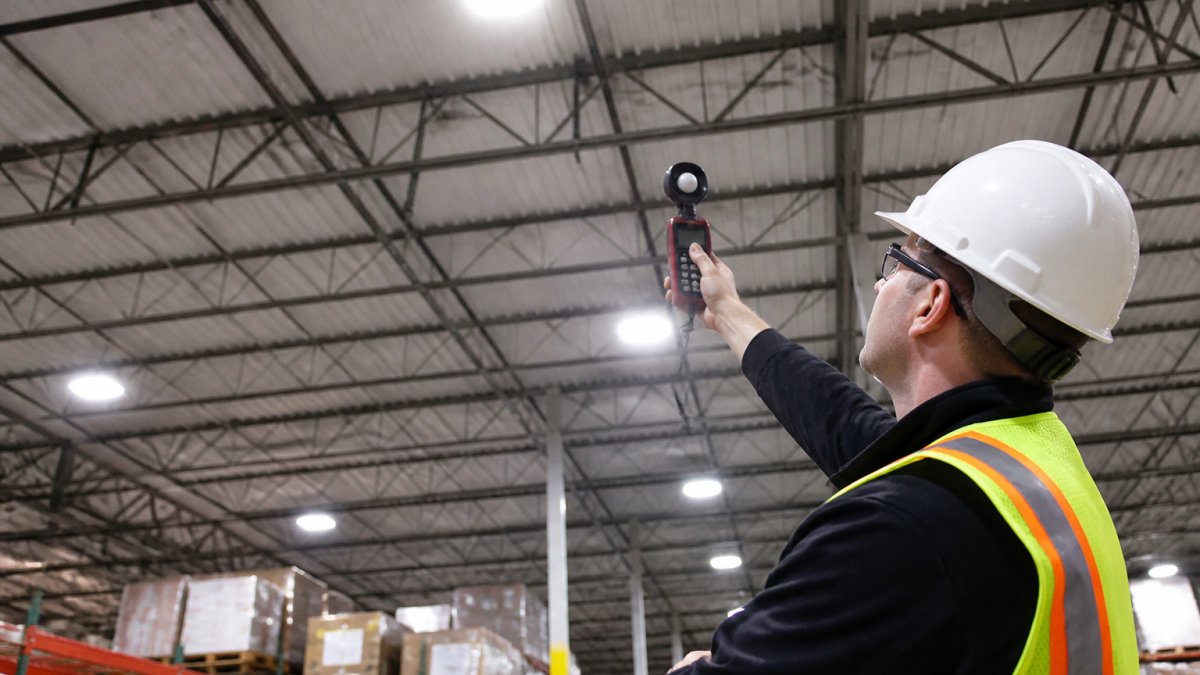 Technician working with energy efficiency consultants to inspect warehouse lighting with a light meter