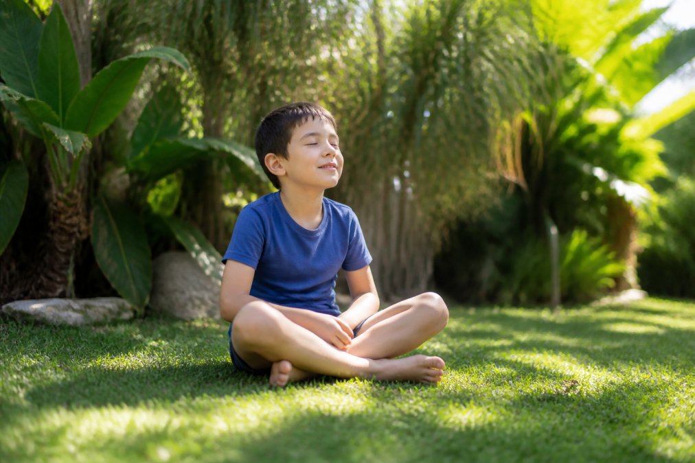 Calm child sitting barefoot on grass practicing energy healing for autistic children in the sunlight.