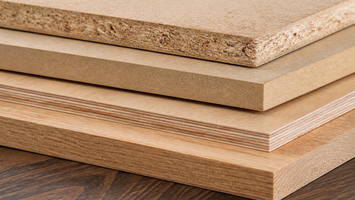 Close-up of different wood panel samples stacked together, showing visible differences in texture, color, and surface finish between particle board, MDF, plywood, and solid wood