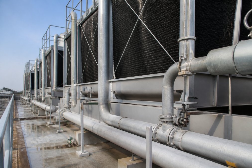 Close-up of industrial cooling tower infrastructure with visible water circulation pipes, thermal management equipment, and operational monitoring systems in daylight