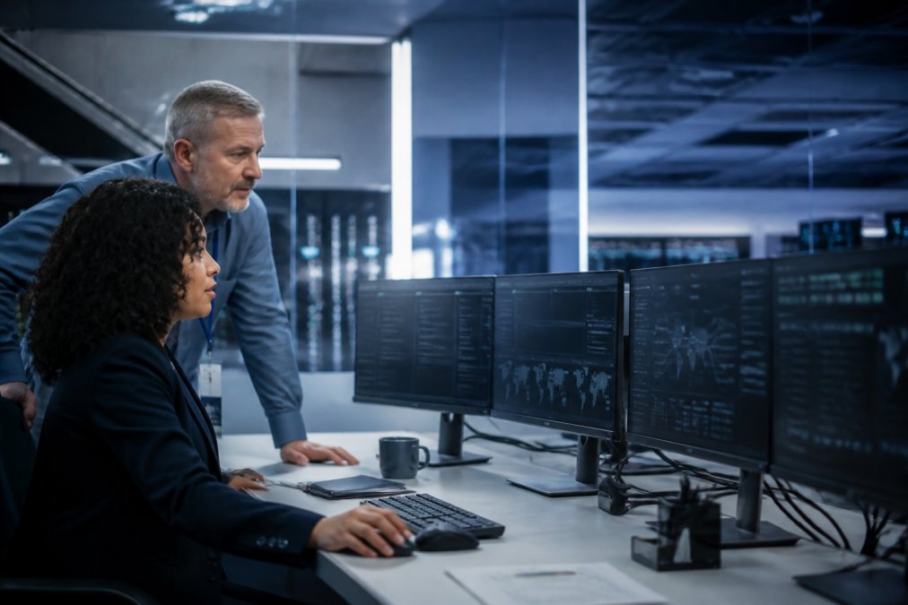 Security architect and AI engineer reviewing agent monitoring dashboards on multiple screens in a modern control room with soft overhead lighting