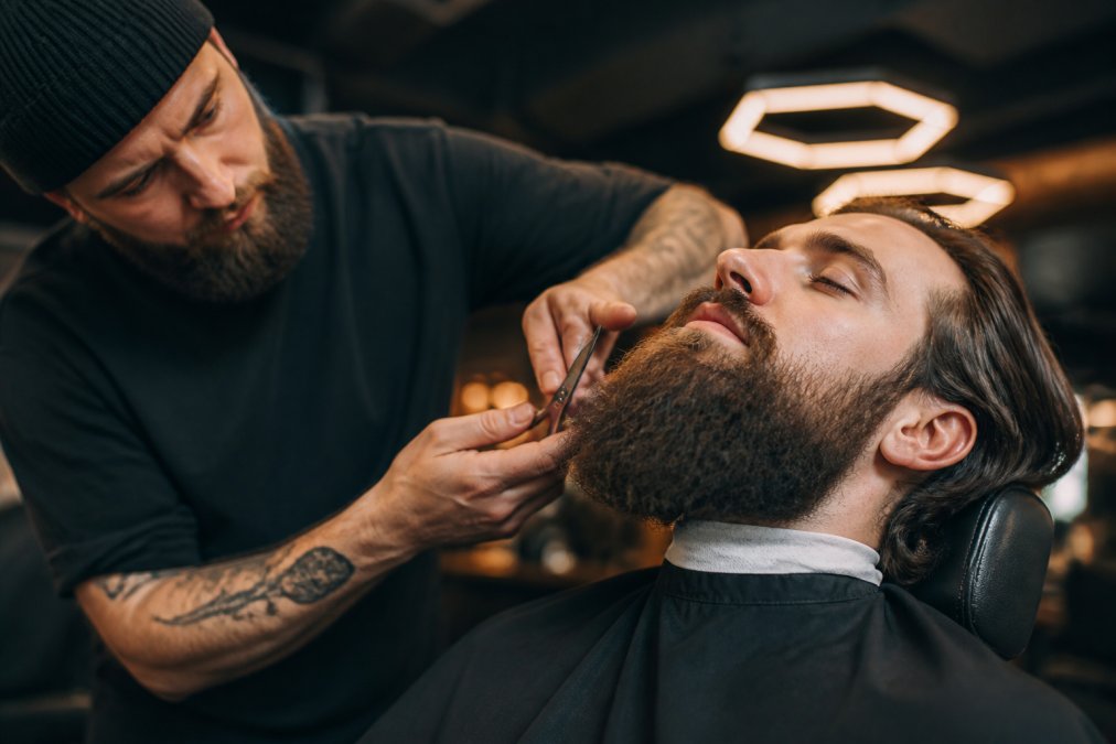 Barbier professionnel utilisant des ciseaux pour effiler et structurer la barbe d'un client, dans un salon moderne et élégant avec un éclairage chaleureux