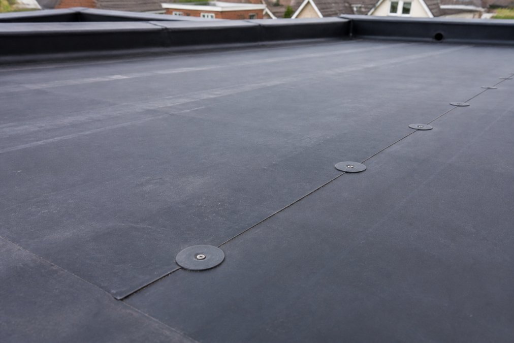 Close-up of black EPDM rubber membrane surface showing the characteristic texture, seams, and fastening details on a residential flat roof installation
