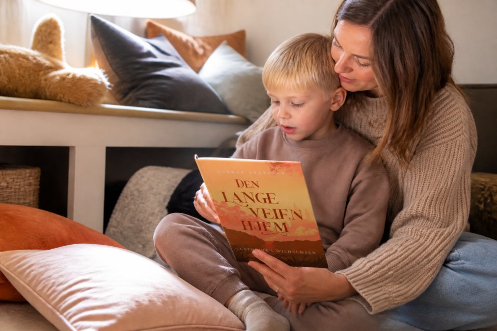 Et barn som leser en illustrert bok sammen med en voksen på en koselig lesekrok med myke puter og varmt lys