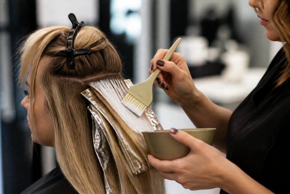Professional colorist applying hand-painted balayage highlights with a feathered tint brush to sectioned blonde hair, demonstrating precise brush control and angled application technique on a client in a modern salon