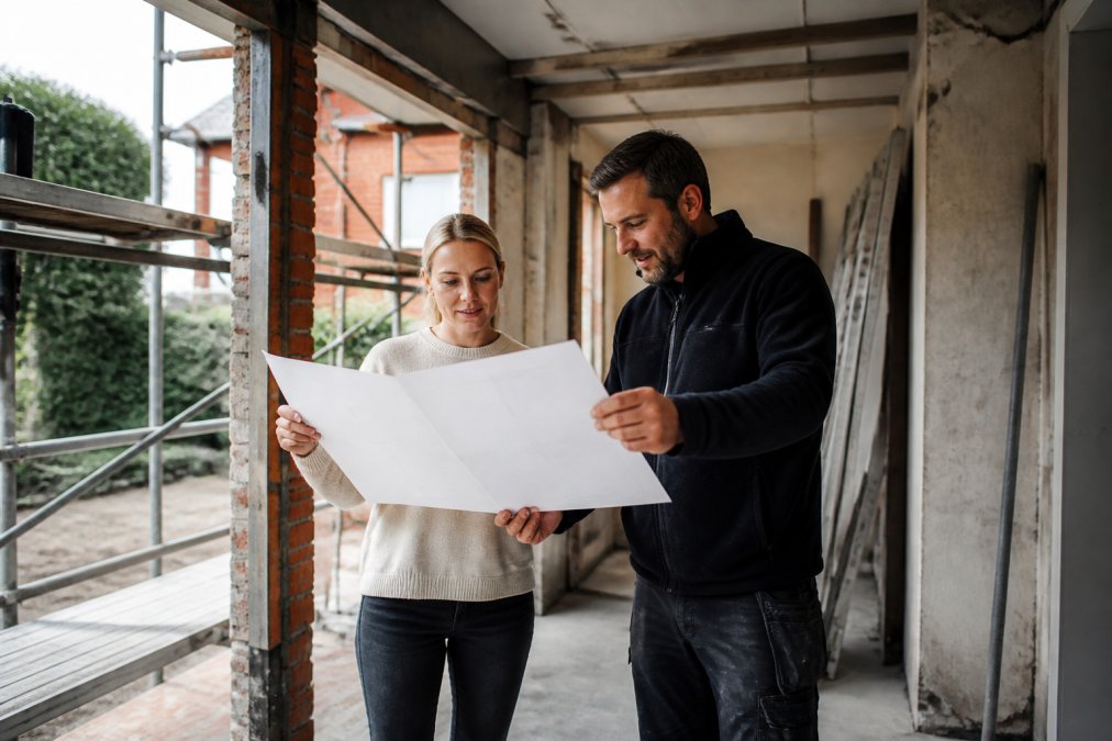 Huiseigenaar in gesprek met een ervaren aannemer voor totaalrenovatie vinden terwijl ze bouwplannen op de werf bekijken.