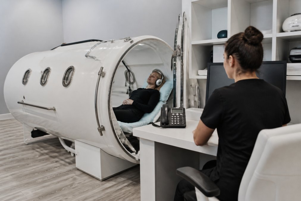 Technician reviewing patient data beside a monoplace hyperbaric oxygen therapy chamber in a modern clinic room