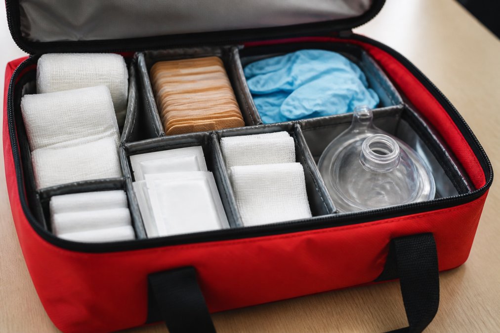 Infographic checklist of essential first aid for businesses featuring medical supplies in organized compartments