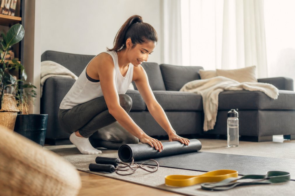 Beginner setting up affordable fitness gear like bands and a yoga mat in a sunlit living room home gym space.