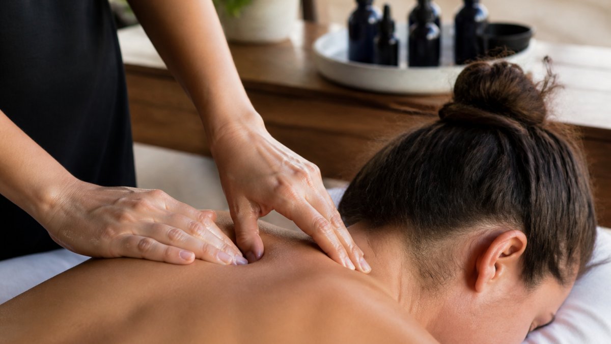 Hands applying a diluted blend of essential oils for muscle relief to a person's neck and shoulders during a massage