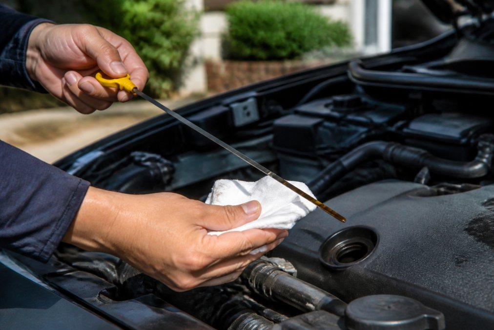 Close-up of hands checking engine oil level with dipstick, showing fluid level markings clearly visible on a sunny day in a driveway
