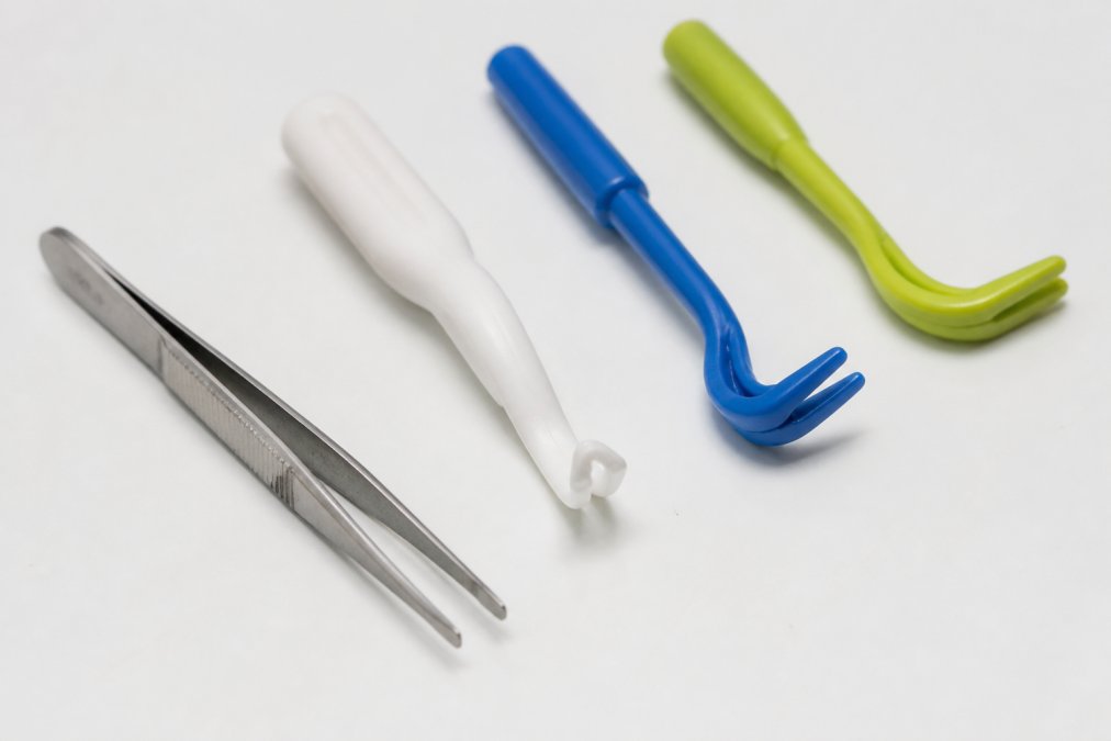 Fine-tipped tweezers and tick removal devices laid out on a clean white surface showing precision tools with clear metal details and ergonomic handles
