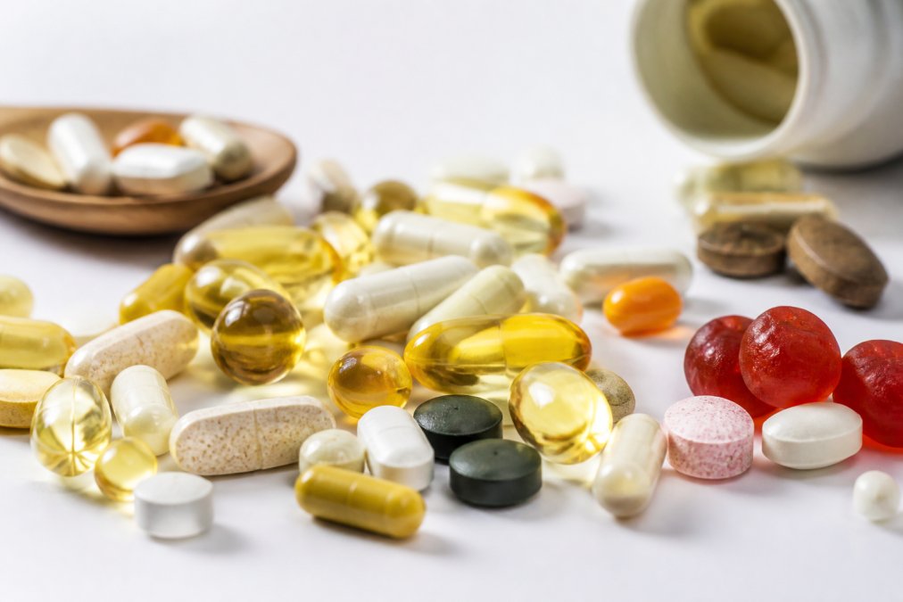 Close-up of colorful supplement capsules, tablets, and gummies arranged on a bright white surface with natural lighting, showing variety of wellness products