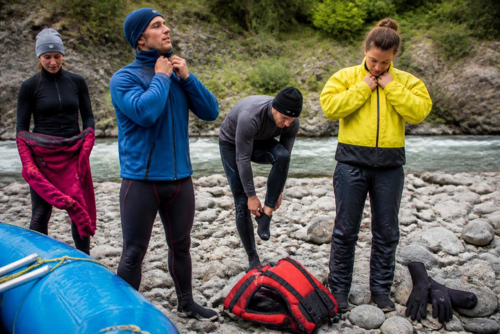 Rafters putting on essential whitewater rafting gear for cold water including fleece layers and splash jackets.