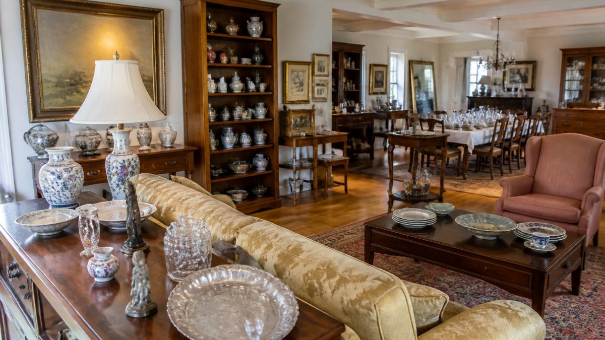 Wide-angle view of a home's interior with organized furniture, artwork, and collectibles displayed on shelves and walls, showing the scale and variety typical of an estate sale setup