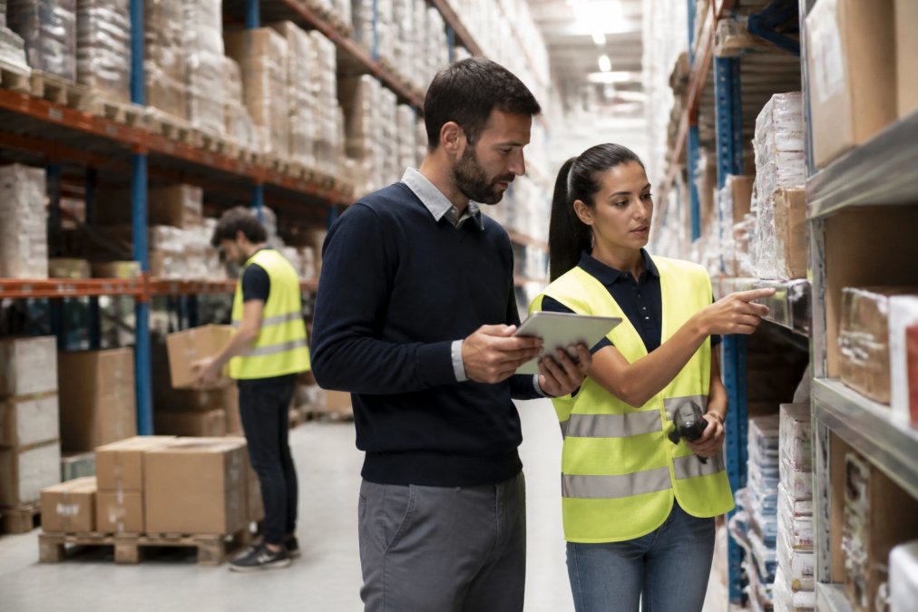 Operatori logistici qualificati che lavorano in un magazzino moderno, con scaffalature industriali sullo sfondo e un responsabile che supervisiona le attività di gestione scorte in un ambiente ben illuminato