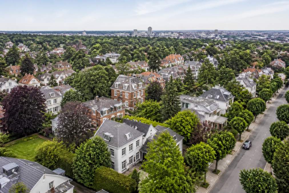 Perspective aérienne montrant la diversité architecturale et les espaces verts d'Uccle, avec des maisons résidentielles de styles variés et des rues bordées d'arbres