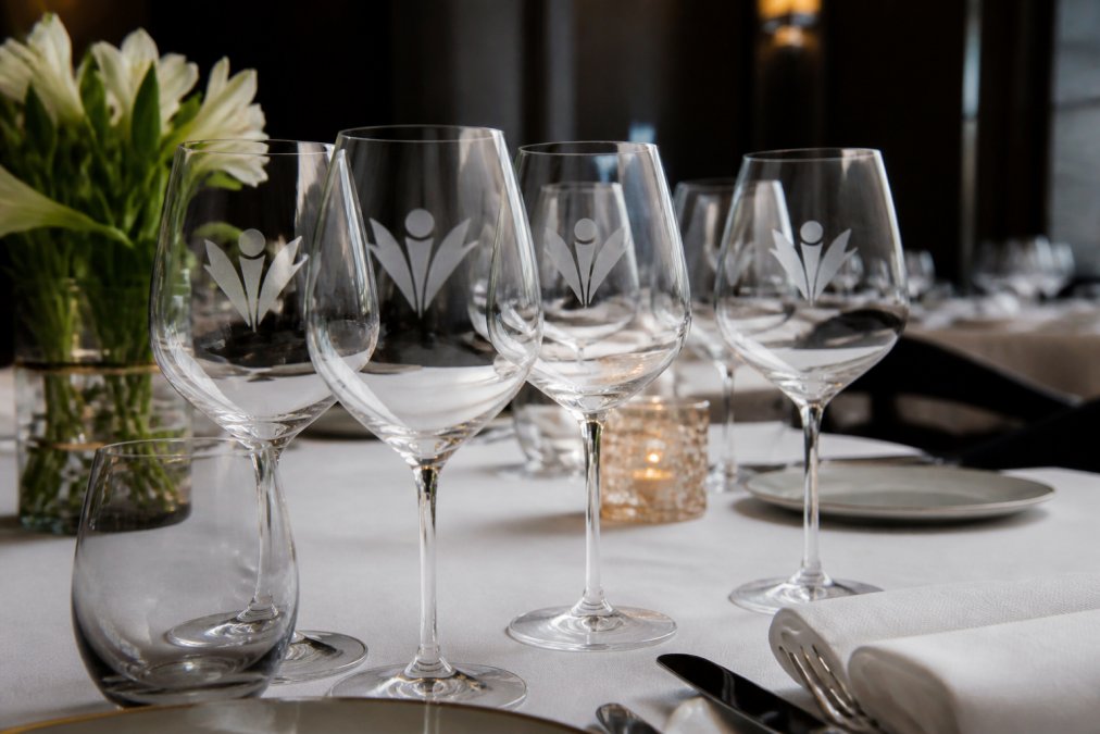 Set of premium wine glasses with etched logos arranged on elegant hospitality table setting with white linens and soft ambient lighting, showing professional presentation and sophisticated frosted branding