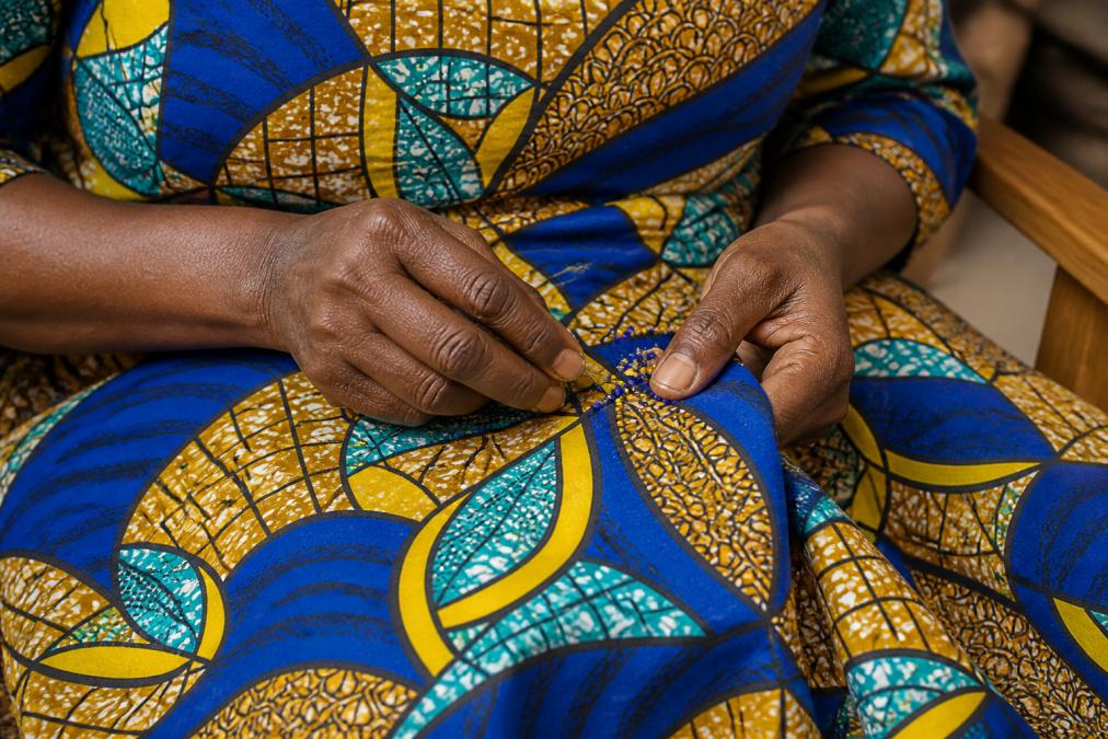 Close-up of skilled artisan hands beading an intricate African textile piece with natural lighting, showing detailed beadwork and traditional patterns