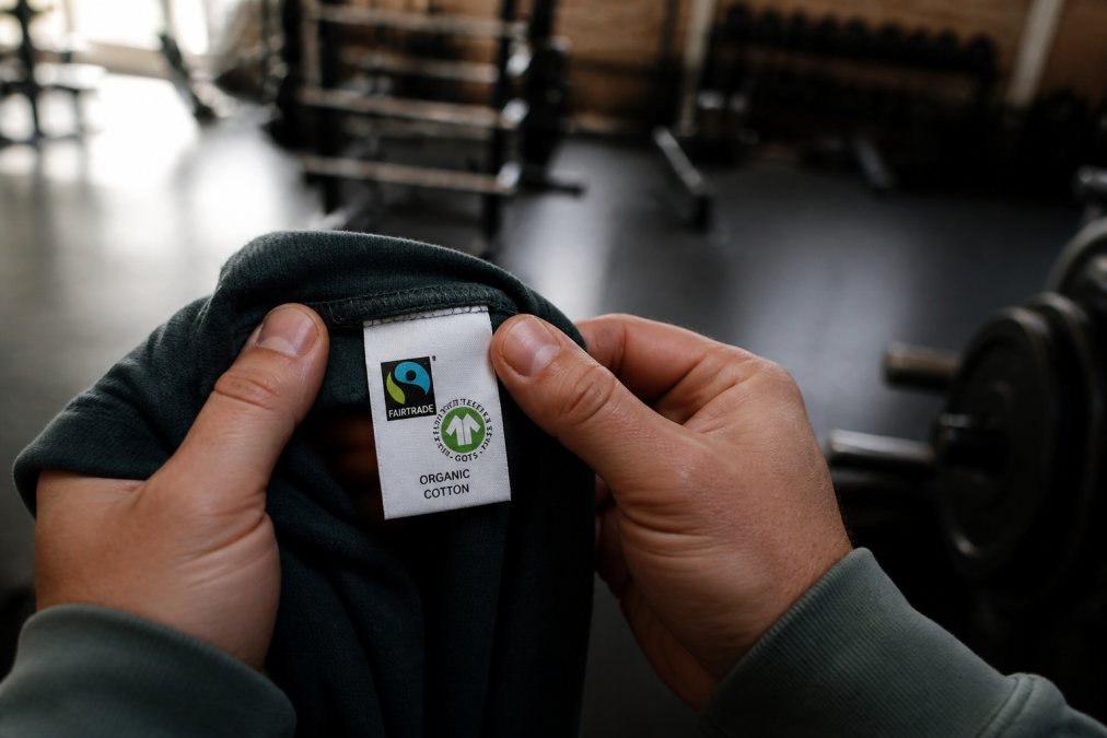 Athlete holding a garment tag featuring fair trade and organic cotton labels in a gym
