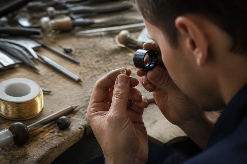 Jeweler using a loupe to inspect an antique diamond, demonstrating ethical craftsmanship at the workbench.