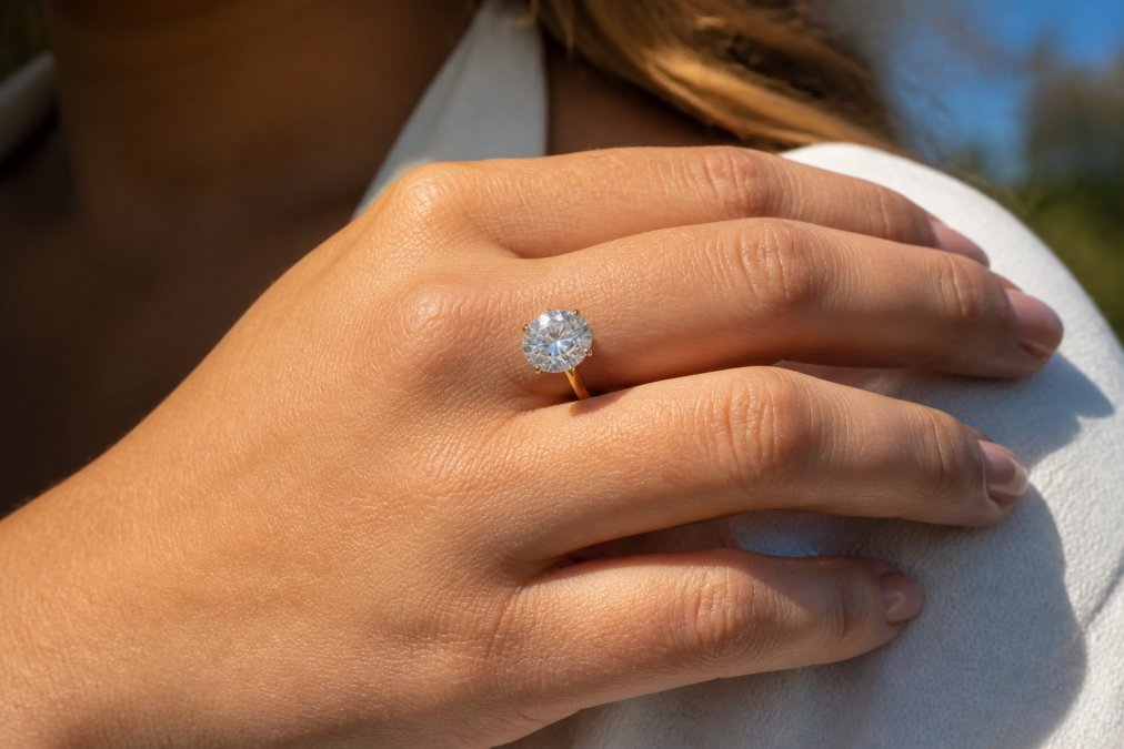 Close-up of a woman's hand wearing an elegant diamond ring in natural sunlight, the stone's sparkle and facets clearly visible with soft diffused lighting highlighting the stone's brilliance