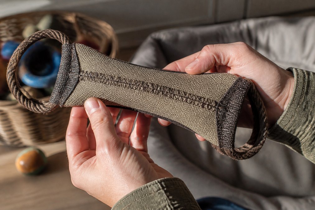 A durable dog toy being held and inspected in hands, showing strong stitching, reinforced seams, and quality construction with natural lighting highlighting the craftsmanship