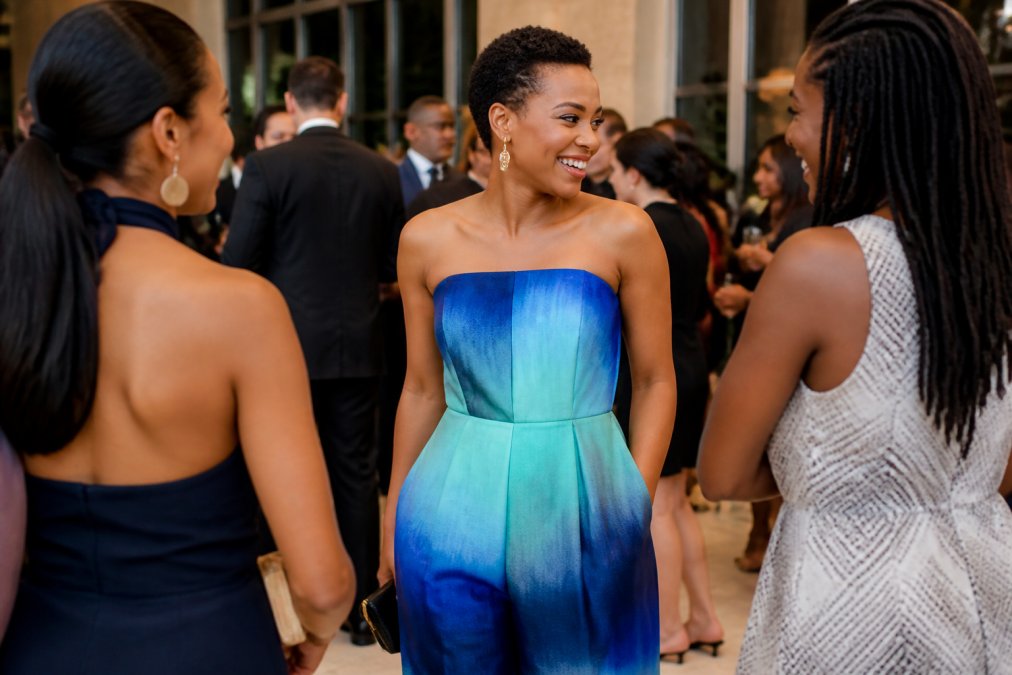 Woman wearing an elegant blue ombré strapless jumpsuit at a formal evening event, showcasing the handcrafted textile details and luminous gradient effect under soft ambient lighting
