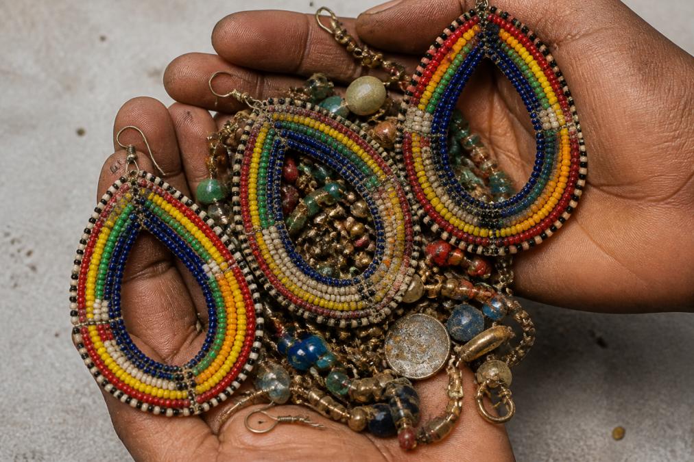 Close-up of hands holding a collection of mass-produced jewelry pieces showing visible tarnishing, broken clasps, and worn finishes, arranged on a neutral surface with harsh lighting highlighting the poor quality