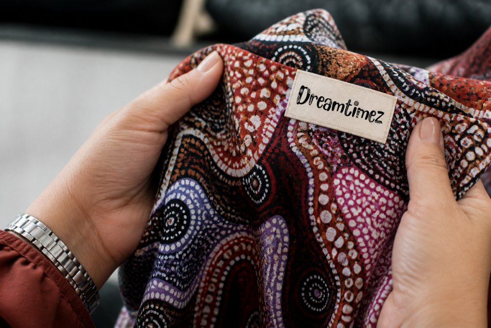Close-up of hands holding a beautifully designed Indigenous-patterned scarf or garment, showing the fine detail and craftsmanship of authentic Aboriginal textile work