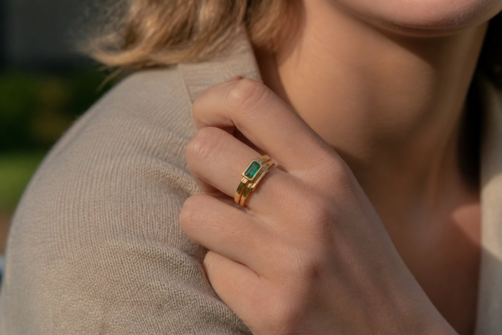 Close-up of a woman's hand wearing an elegant recycled gold ring with an emerald stone, showcasing intricate architectural design details and craftsmanship