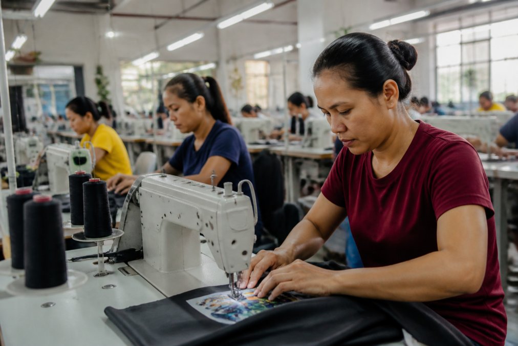 Skilled garment workers at sewing stations in a well-lit, organized manufacturing facility with proper workstations