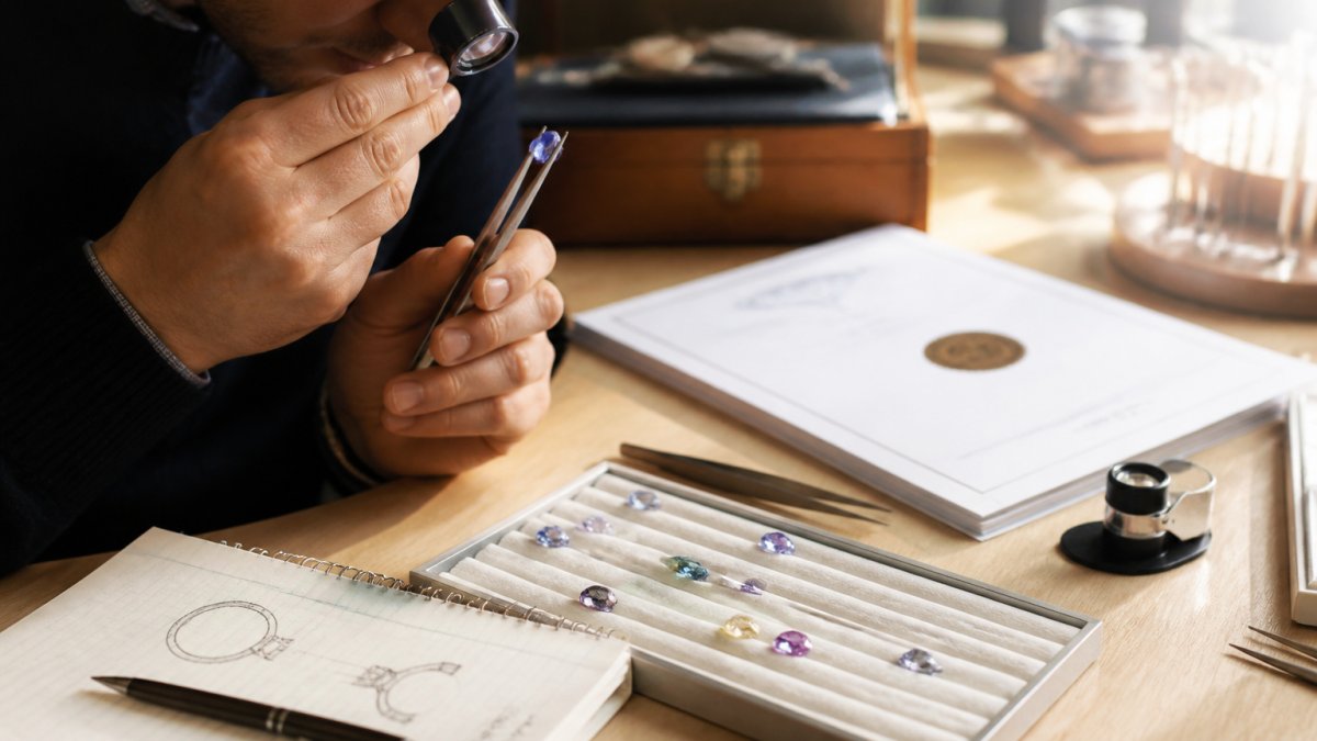 Jeweler examining loose gemstones with a loupe near certification papers to ensure ethical material sourcing.