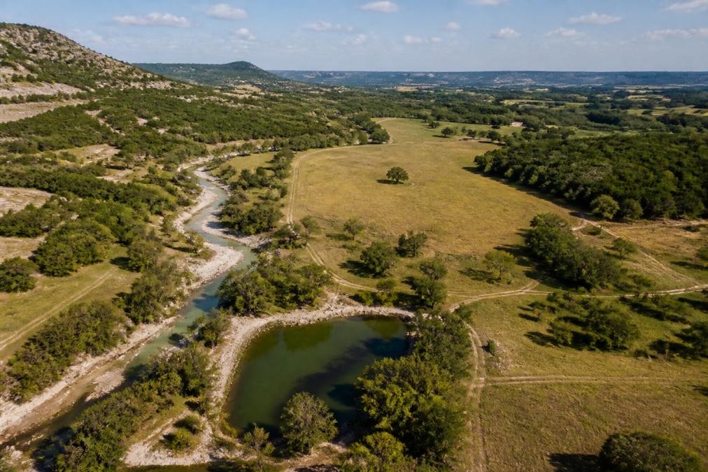 Aerial view of ranch landscape with visible water sources, creek beds, pasture areas, and topographical variation showing elevation changes across property