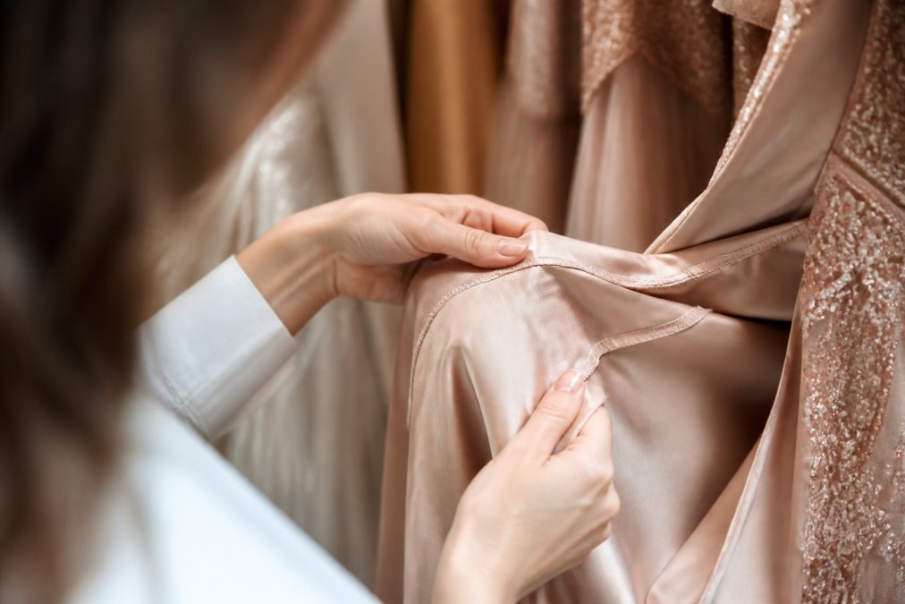 Hands inspecting the high-quality inner lining and seams of luxury evening gowns online with soft natural light