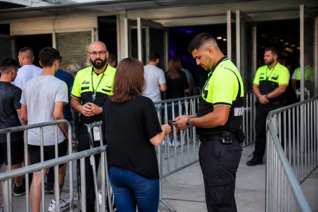 Professional security guards in high-visibility uniforms stationed at multiple entry and exit points of a modern venue, monitoring crowd flow and checking identification during an event