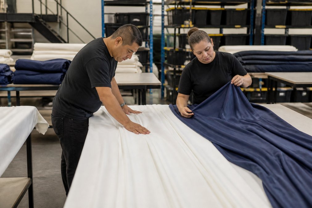 Professional crew members carefully inspecting pristine white and navy drapes laid out on clean tables, examining fabric texture and seams under bright studio lighting